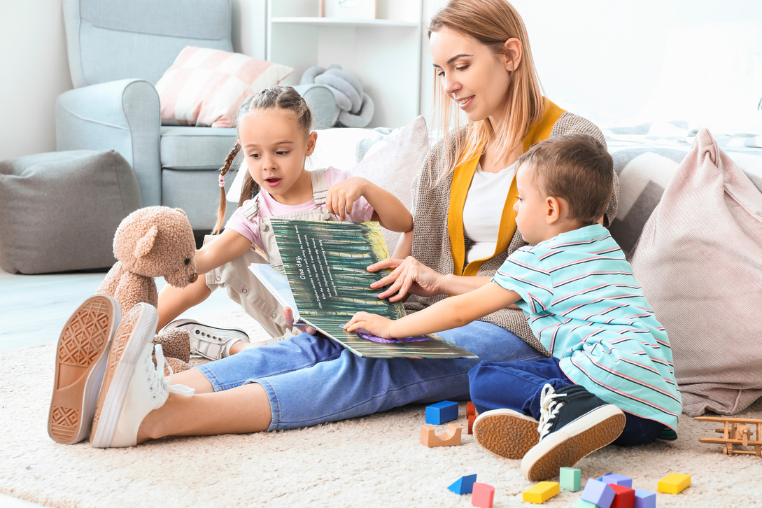 Nanny and Cute Little Children Reading Book at Home